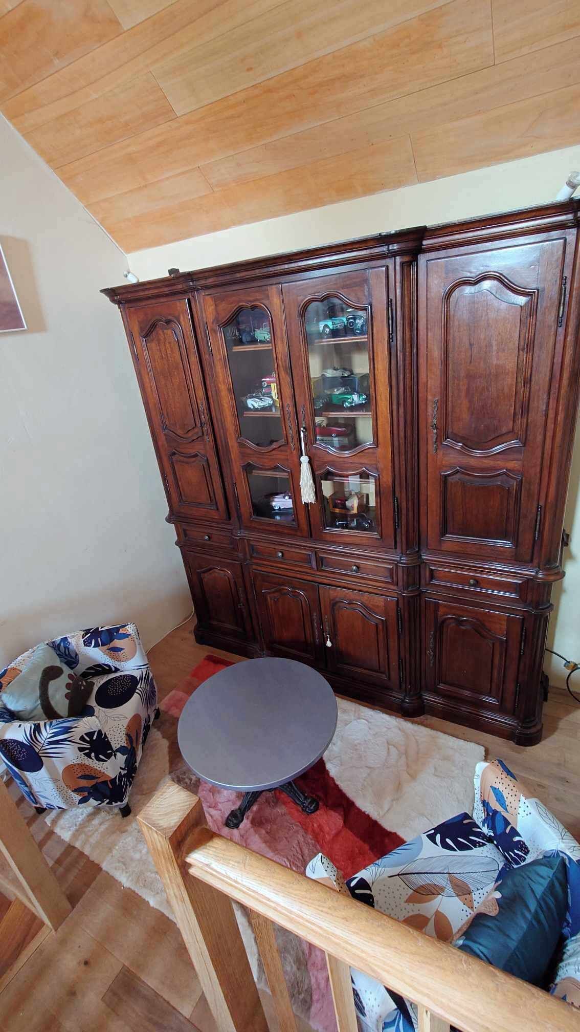 Una habitación con un armario de madera, una mesa redonda y un sillón estampado.