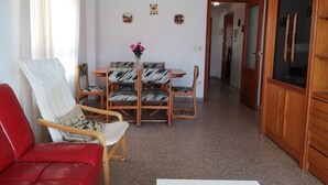 Ein Wohnzimmer mit einem roten Sessel, einem Holzespeisetisch mit gemusterten Stühlen, einem weißen Sofa und einem Schrank.