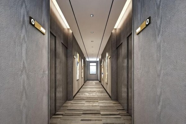 A long, narrow hallway with a patterned floor, walls with textured panels, and overhead lighting. - Qinyu Hotel (Haikou)