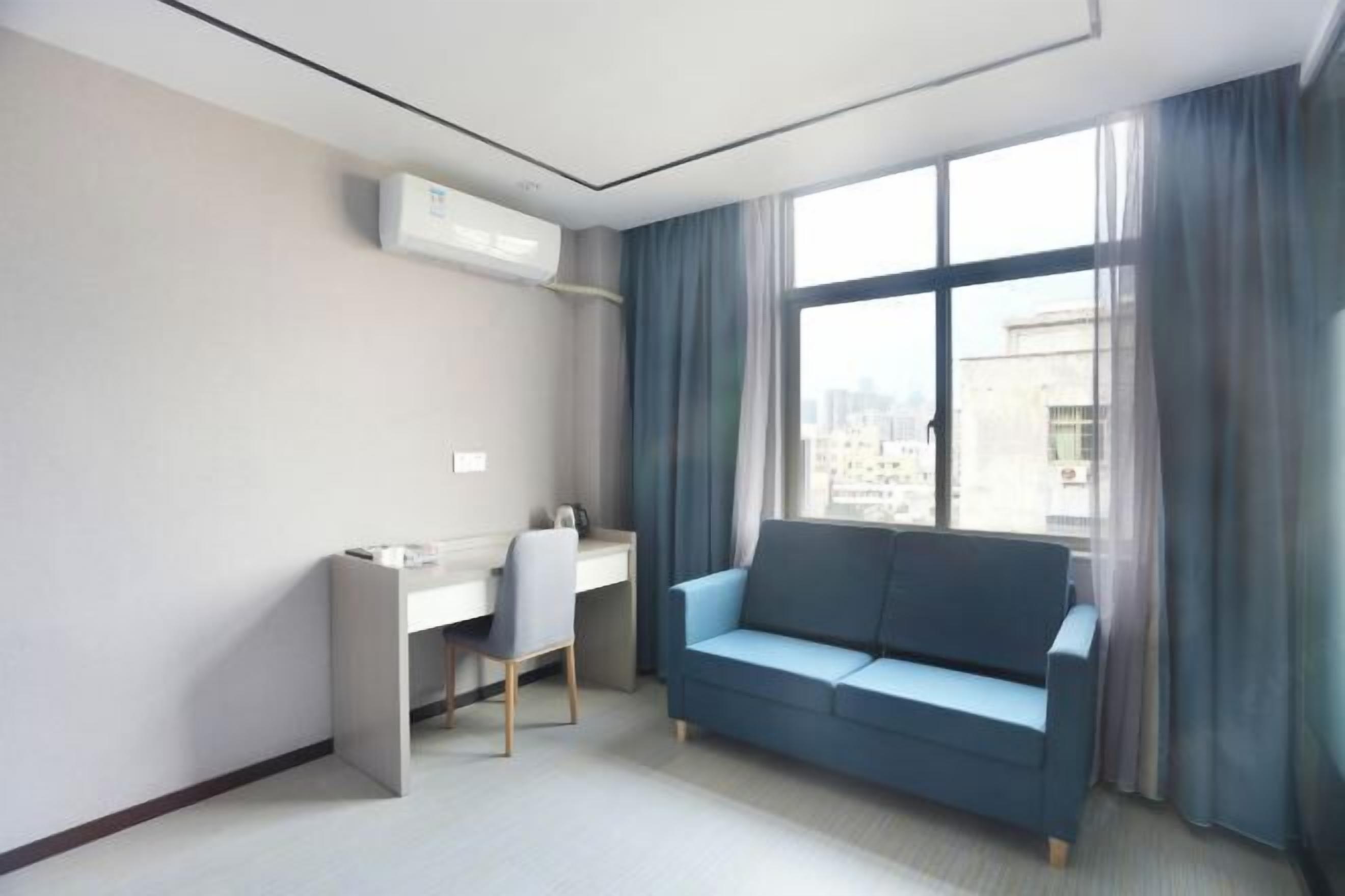 A modern hotel room with a desk, a blue sofa, and a large window with curtains.