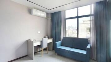 A modern hotel room with a desk, a blue sofa, and a large window with curtains.