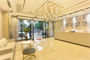 Un espace d’accueil d’hôtel doté d’une entrée avec porte vitrée, d’un comptoir de réception et de plusieurs sièges.