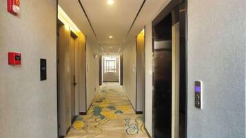 A hotel hallway with a carpeted floor, doors on both sides, and a light fixture on the ceiling.