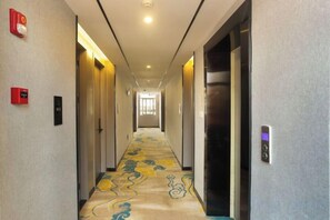 Un couloir d’hôtel avec un sol recouvert de moquette, des portes de chaque côté et un luminaire au plafond.