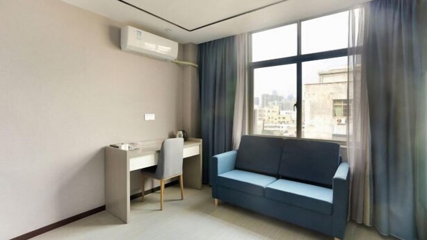 A modern hotel room with a desk, a blue sofa, and a large window offering a city view. - Qinyu Hotel (Haikou)