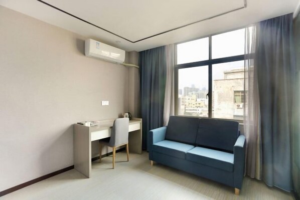 Una habitación de hotel moderna con un escritorio, un sofá azul y un amplio ventanal con vistas a la ciudad.