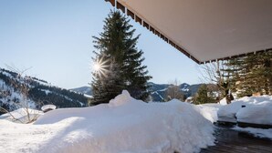 A snow-covered deck with a wooden railing, a snow mound, and a pine tree in the background. - Chalet, view panoramic, terrace, fireplace or stove, parking, tv, ski locker, 168m², La Clusaz (La Clusaz)