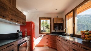 A modern kitchen with wooden cabinets, a red refrigerator, and a window with a mountain view. - Chalet, view panoramic, terrace, fireplace or stove, parking, tv, ski locker, 168m², La Clusaz (La Clusaz)