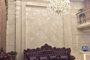 Une pièce dotée d’un grand lustre, d’un canapé moelleux, d’un mur en marbre et d’un téléviseur posé sur un meuble.