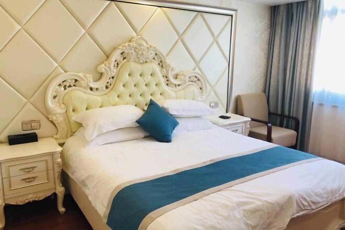 Una habitación de hotel con una cama grande, una mesita de noche, una silla y un cabecero decorativo.