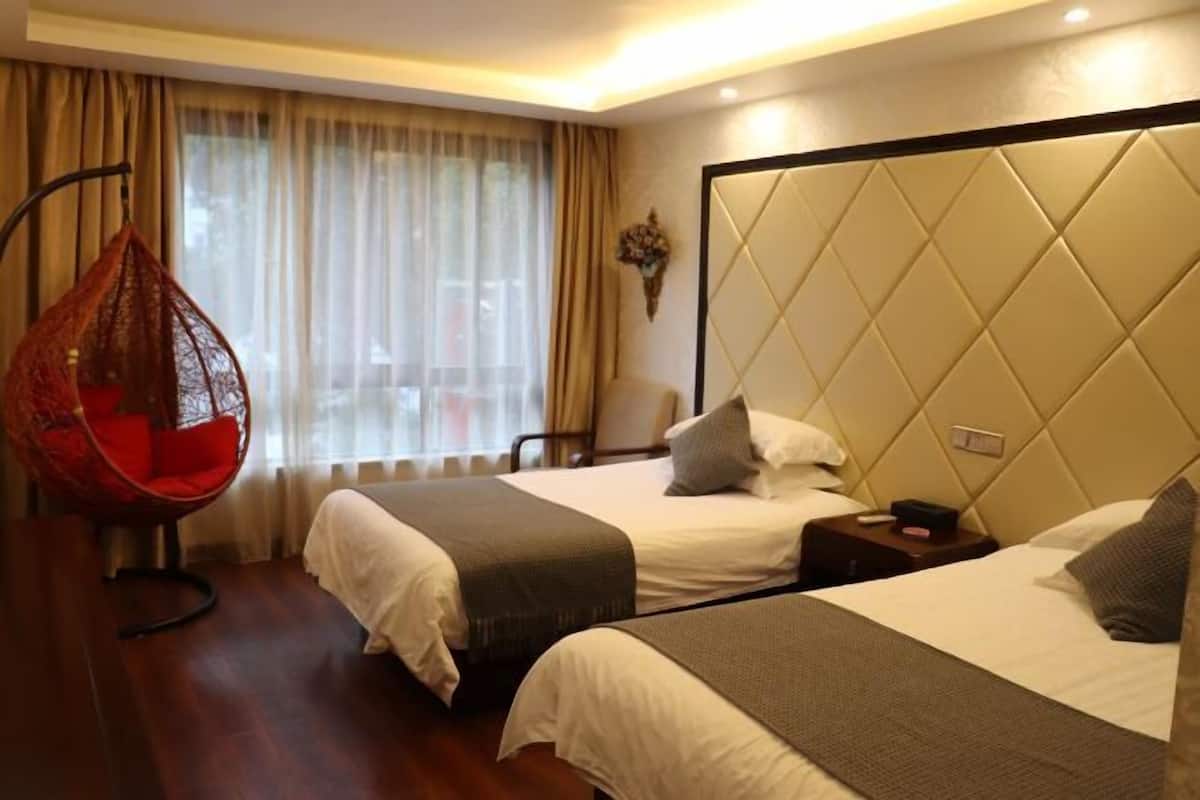 Habitación de hotel con dos camas, un sillón colgante y vistas al exterior a través de cortinas translúcidas.