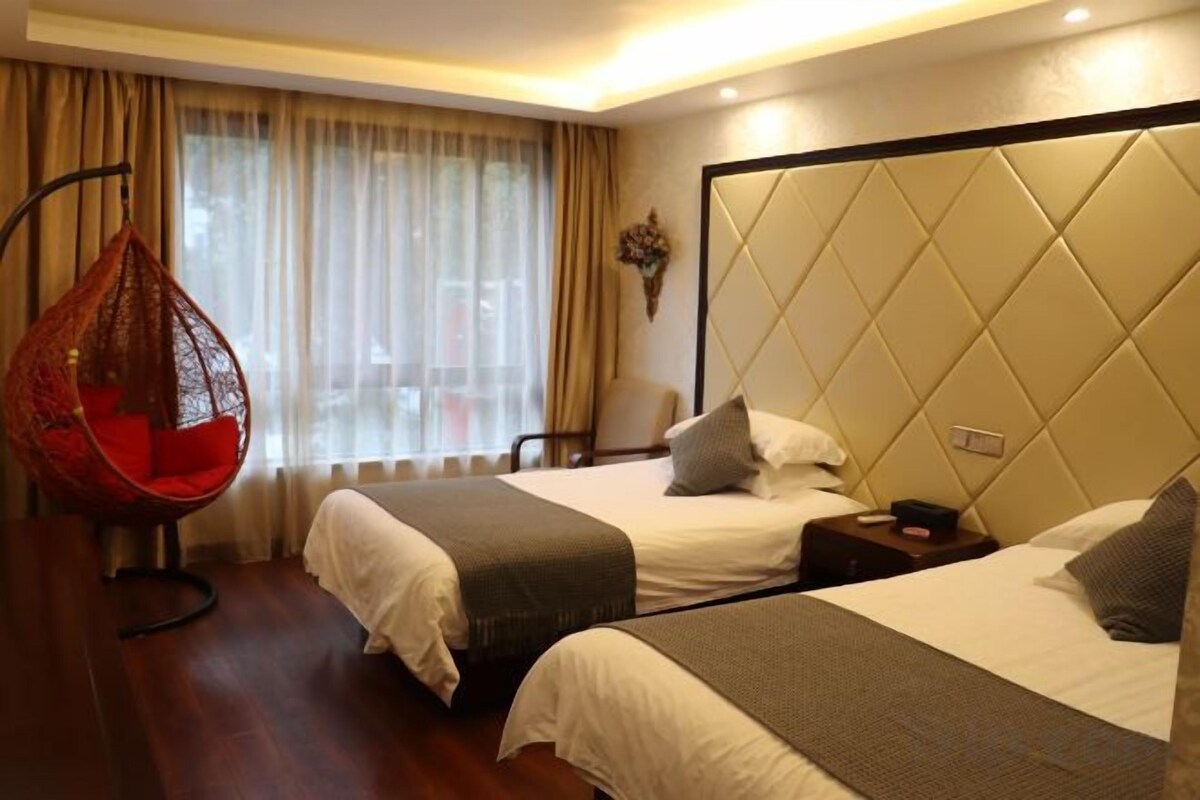 Habitación de hotel con dos camas, una silla colgante, una mesita de noche y un ventanal con cortinas.