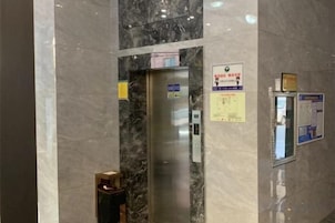 Un ascensor con pared de mármol, detector de incendios y carteles informativos.