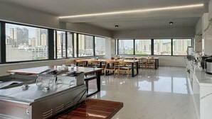 A modern kitchen with a stainless steel sink, wooden tables, and large windows offering city views.