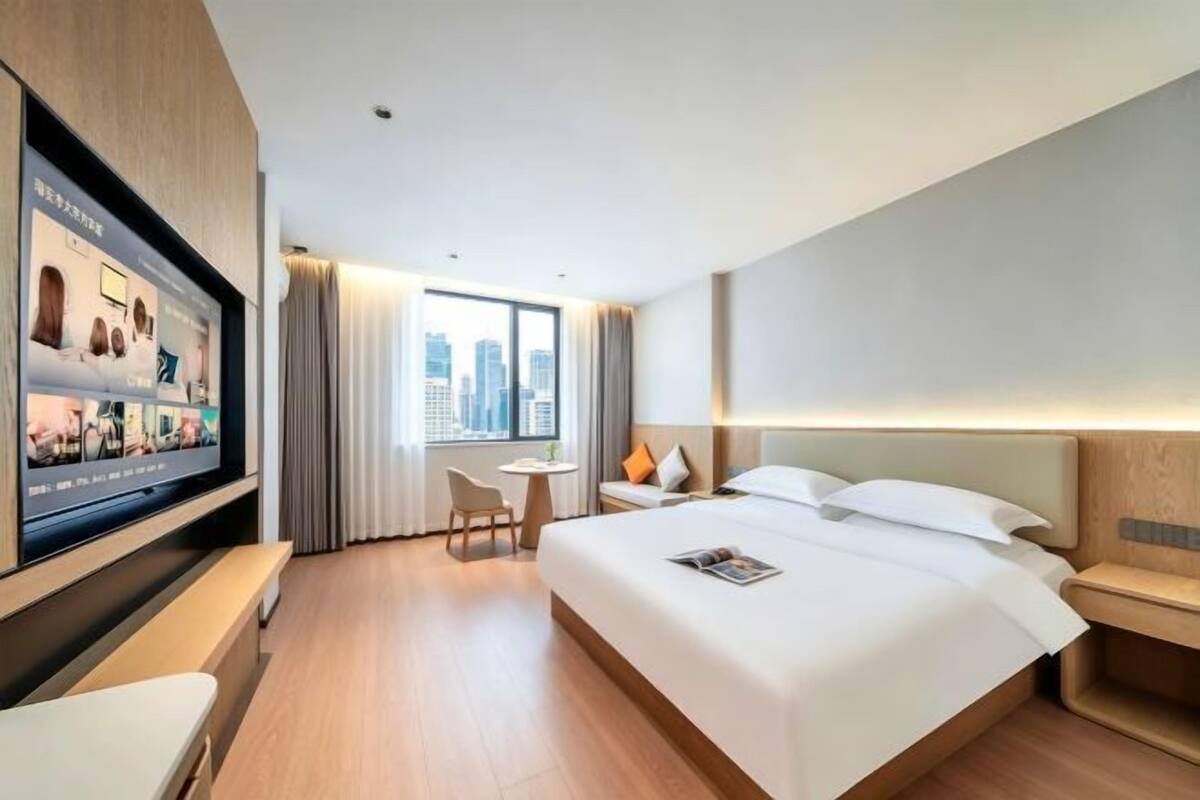 Ein modernes Hotelzimmer mit einem großen Bett, einem an der Wand montierten Fernseher, einem kleinen Tisch und einem Sessel.