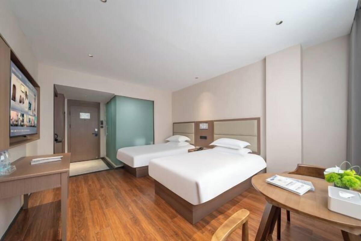 Ein Hotelzimmer mit zwei Betten, einem Schreibtisch, einem Stuhl und einem kleinen Tisch mit einer Pflanze.