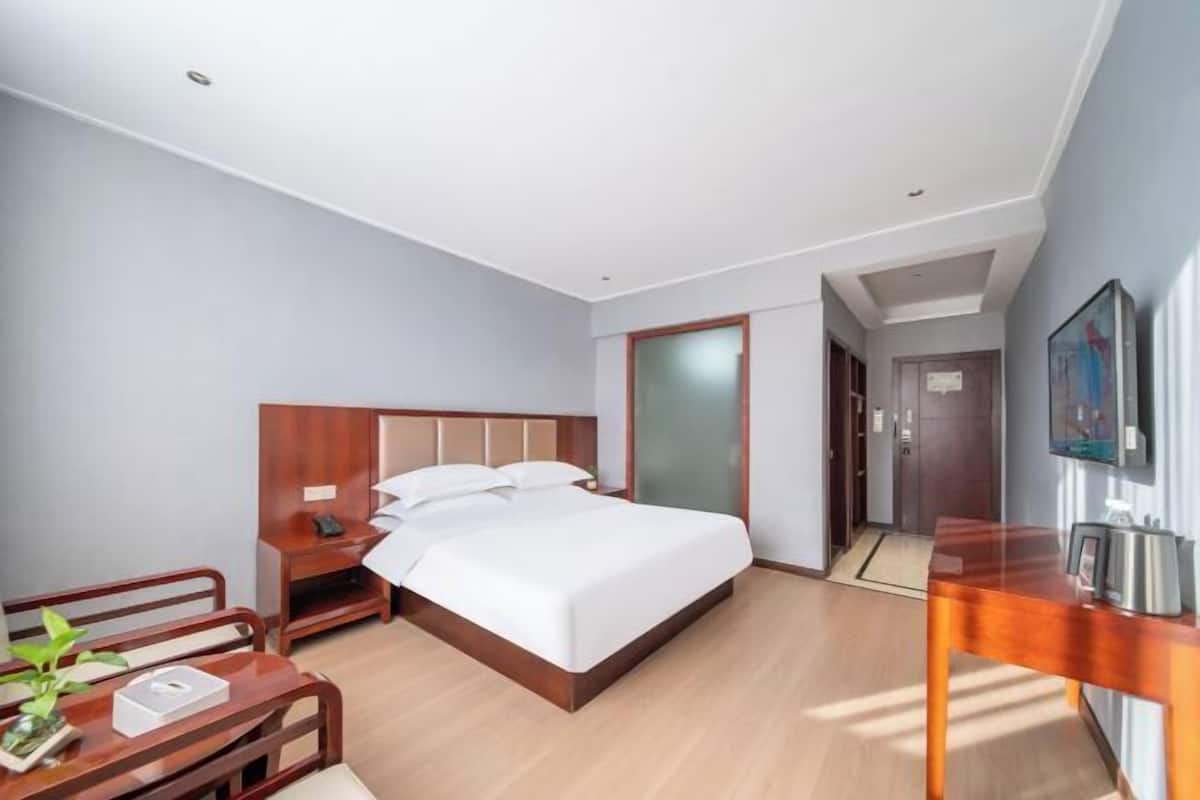 Ein Hotelzimmer mit Bett, Nachttisch, Sessel und Schreibtisch mit Pflanze.