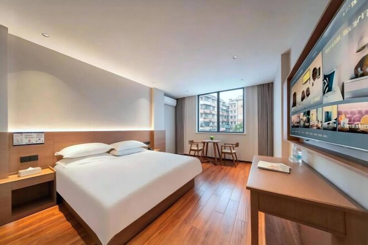 Ein Hotelzimmer mit einem großen Bett, einem Schreibtisch, einem Sessel, einem Fernseher und einem Fenster mit Blick auf die Stadt.