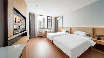 A hotel room with a TV, two beds, a desk, a chair, and a window with a city view.