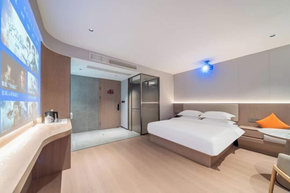 Ein modernes Hotelzimmer mit einem großen Bett, Nachttischen, einem Schreibtisch und einem digitalen Bildschirm, der Inhalte anzeigt.