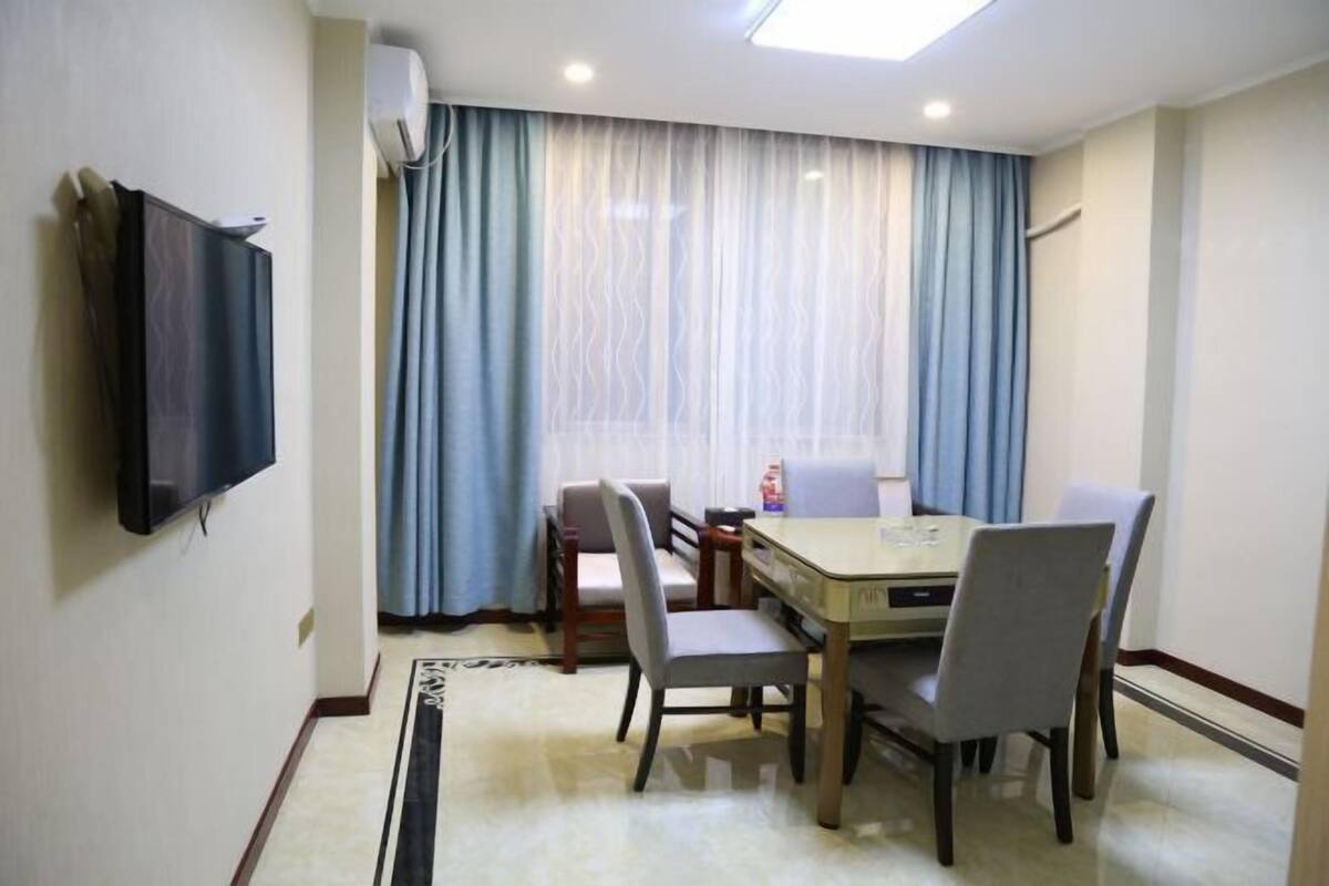 Ein Hotelzimmer mit Esstisch, Stühlen, einem flachbildfernseher an der Wand und einem großen Fenster mit Vorhängen.