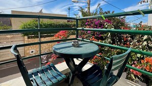 A balcony with a round table and two chairs, surrounded by green railings and flowering plants. - Appartement à 10min des Plages et Souks. Amis à 4 Pates Acceptés ! (Agadir)