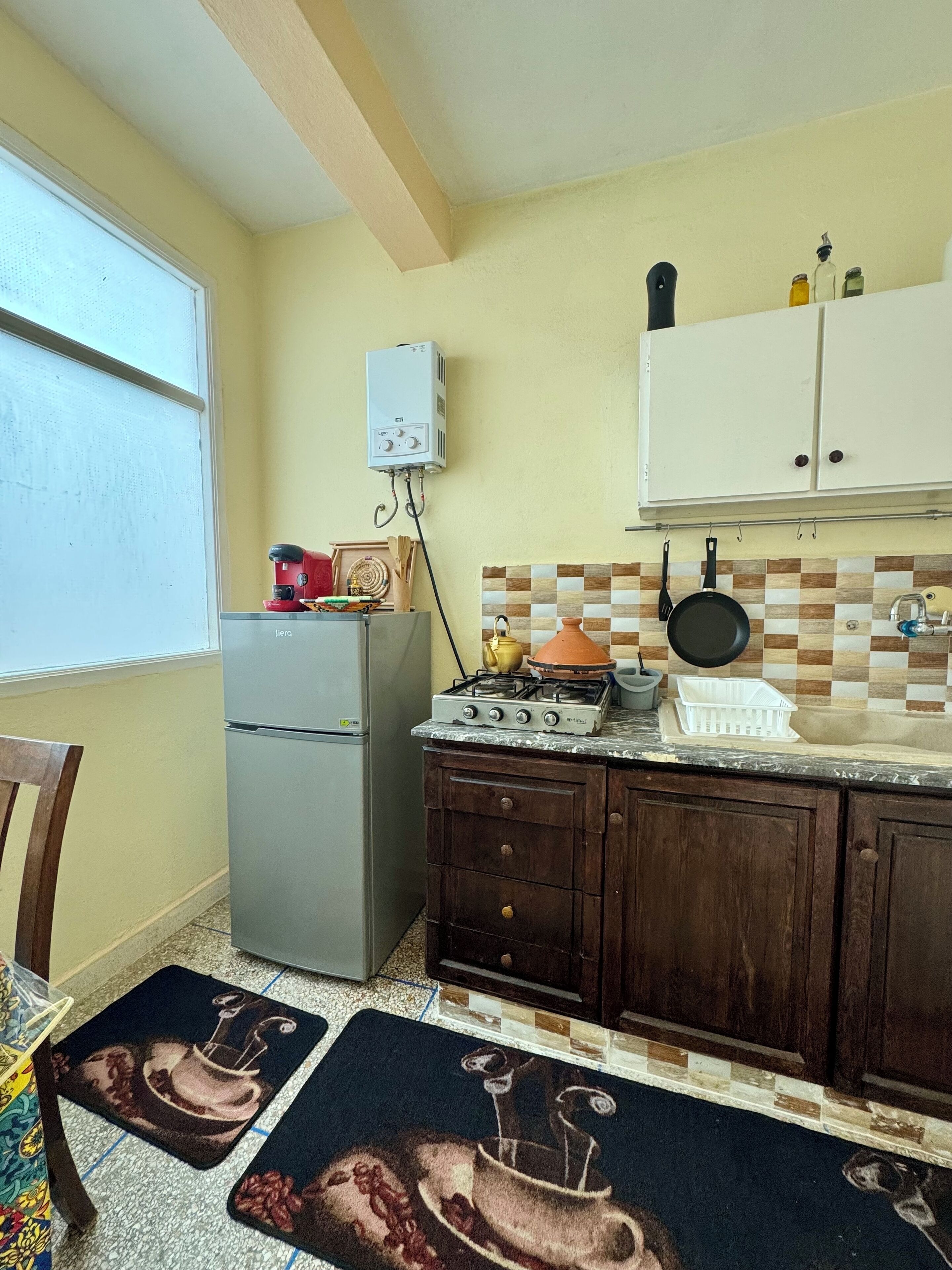 A compact kitchen with a refrigerator, stove, and white cabinets. There is a window and a door leading to another room.