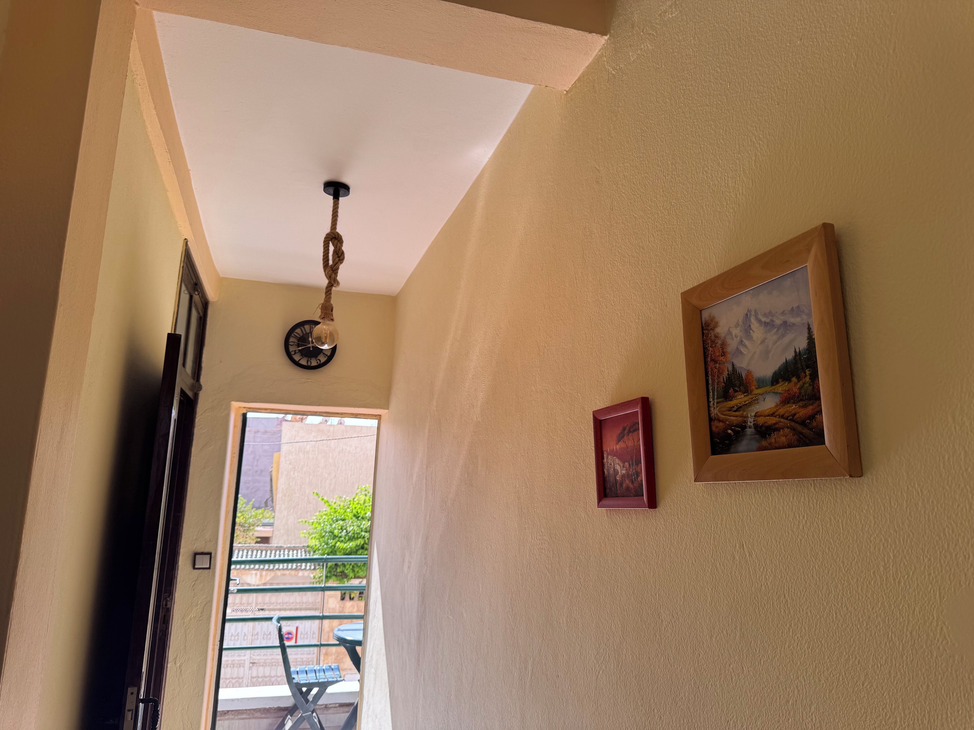 Un pasillo con una lámpara en el techo, un reloj y un cuadro enmarcado en la pared.