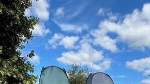 Two tents set up in a grassy field with trees and a clear sky in the background. - Fossewold Camping Bell Tent 1 of 4 (Blockley)