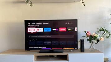 Ett modernt vardagsrum med en platt-TV placerad på en vit TV-bänk, ett jordglob och dekorativa växter.