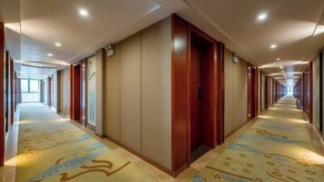 Un couloir d’hôtel avec des portes des deux côtés, une moquette à motifs et un long couloir menant à un espace lumineux.