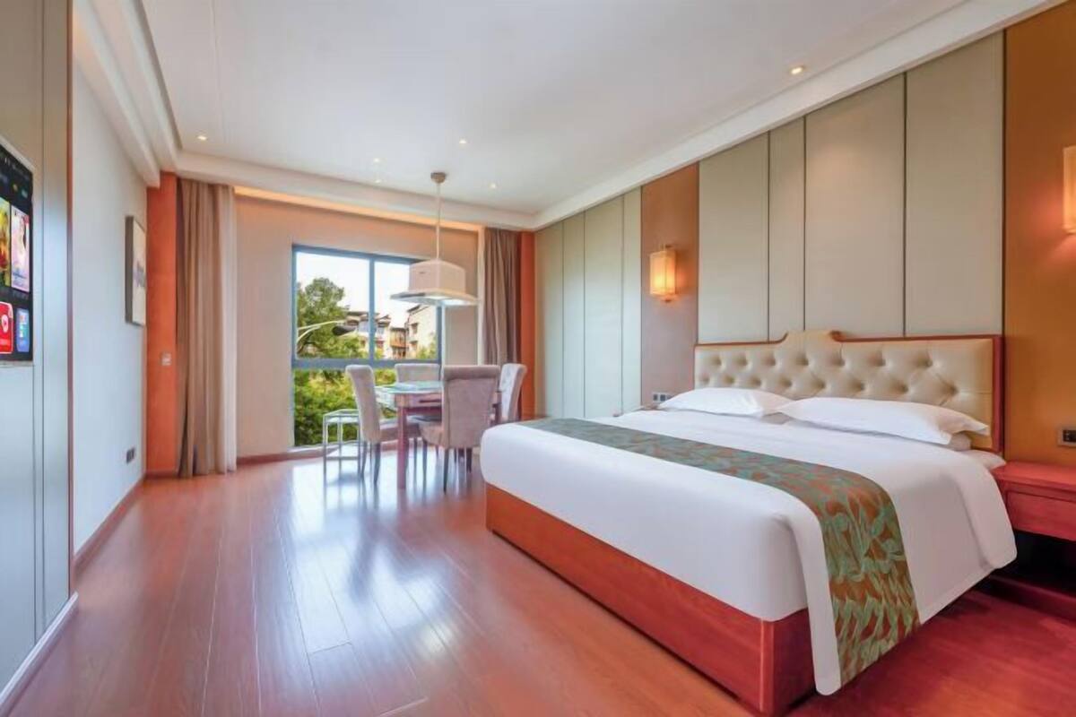 Ein Hotelzimmer mit einem großen Bett, einem Essbereich mit Tisch und Stühlen sowie Blick auf Grünflächen.