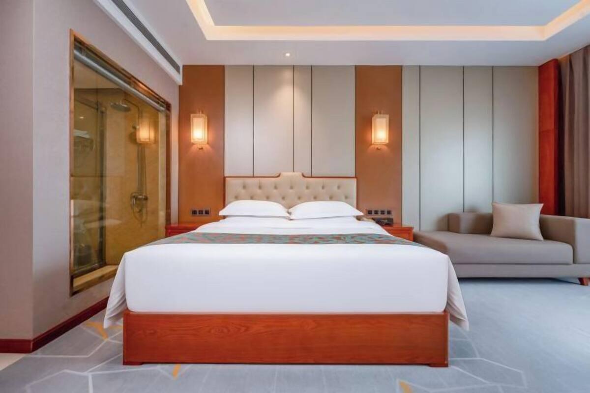 Ein modernes Hotelzimmer mit einem großen Bett, einer Couch, einer Duschkabine aus Glas und einem Holzboden.