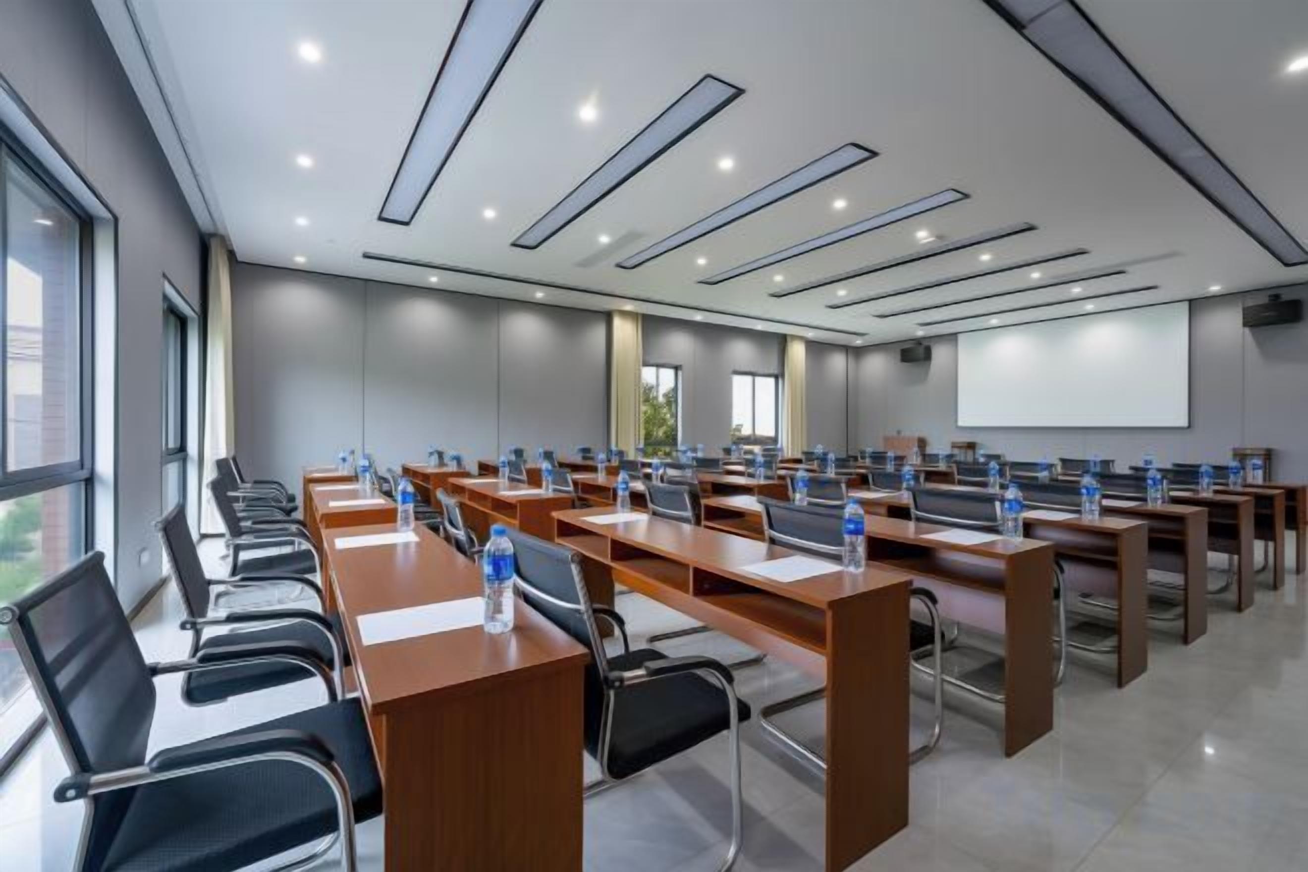 A conference room with multiple tables and chairs, equipped with water bottles, and a projector screen.