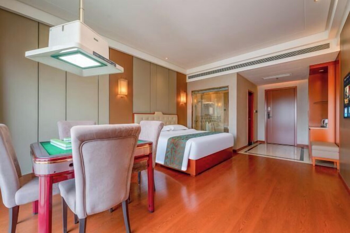 A hotel room with a bed, a desk with a chair, a table with chairs, and a large window.