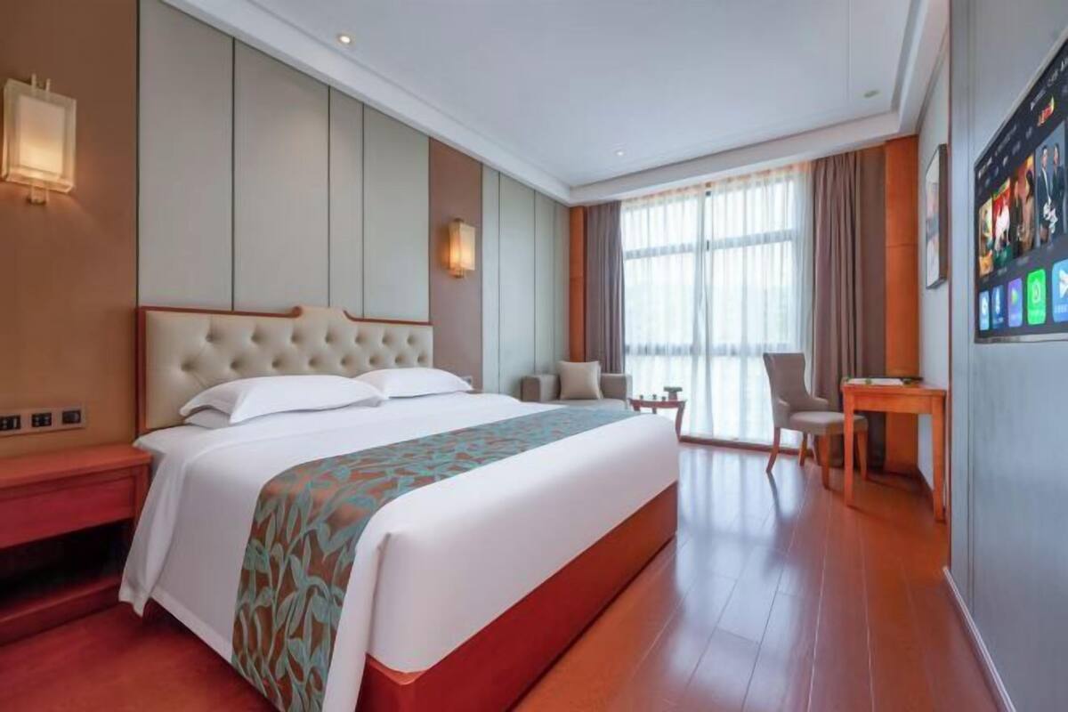 Ein Hotelzimmer mit einem großen Bett, einem Schreibtisch, einem Stuhl und einem Fernsehbildschirm.