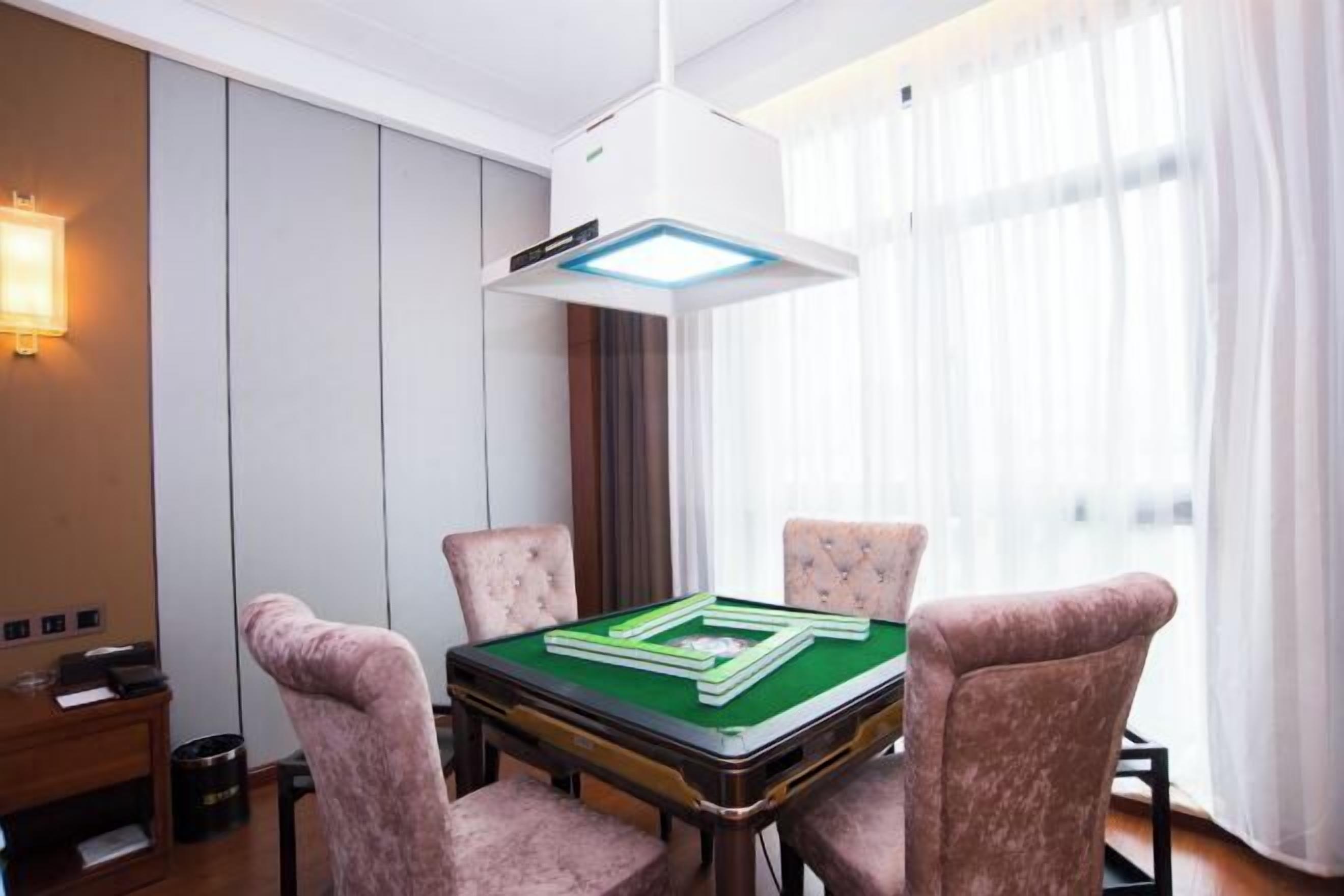 A room with a green pool table, four cushioned chairs, a white ceiling light, and a window with sheer curtains.
