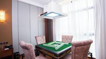 A room with a green pool table, four cushioned chairs, a white ceiling light, and a window with sheer curtains.