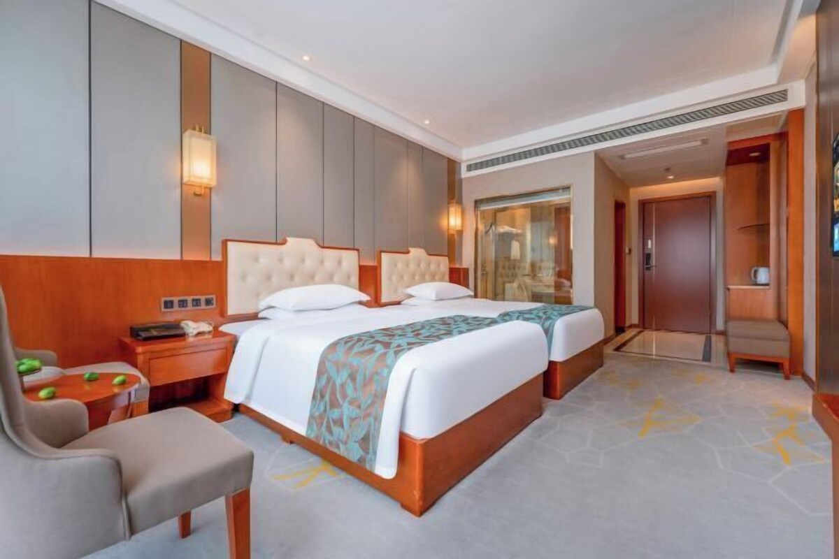 A hotel room with two beds, a desk, a chair, a bedside table, and a large mirror.
