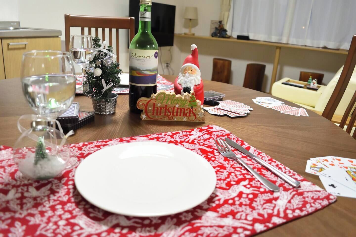 A dining table set with a Christmas ornament, a bottle, and playing cards.