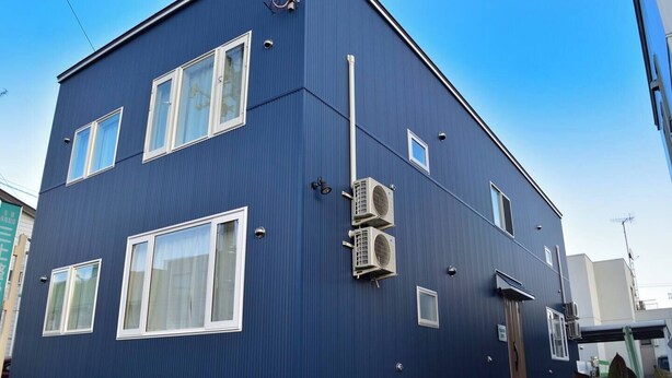 Ein zweistöckiges Gebäude mit blauer Fassade, zahlreichen Fenstern und Klimaanlagen.