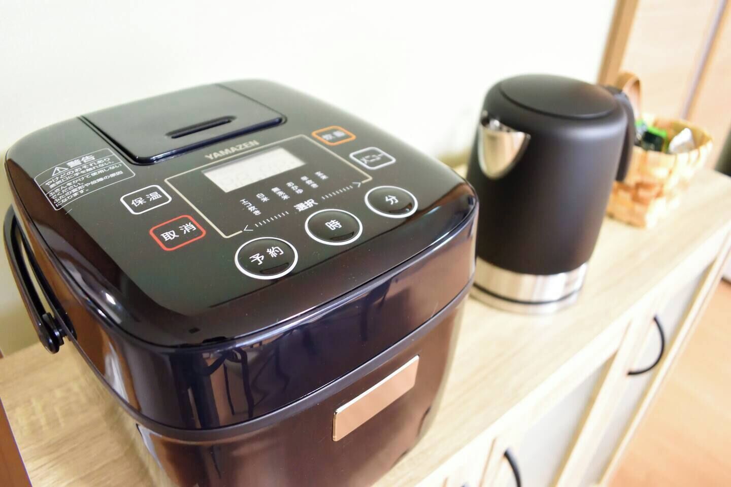 A black rice cooker with a digital display and control buttons on a wooden countertop.