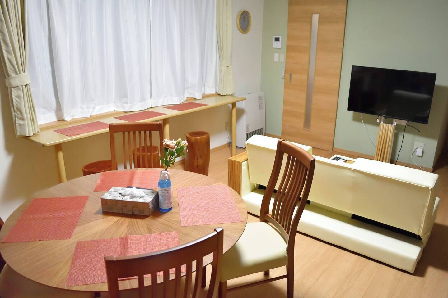 A room with a round dining table, chairs, a sofa, a TV, and a window with curtains.
