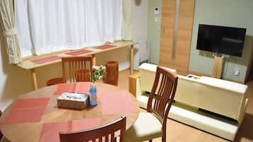 A room with a round dining table, chairs, a sofa, a TV, and a window with curtains.