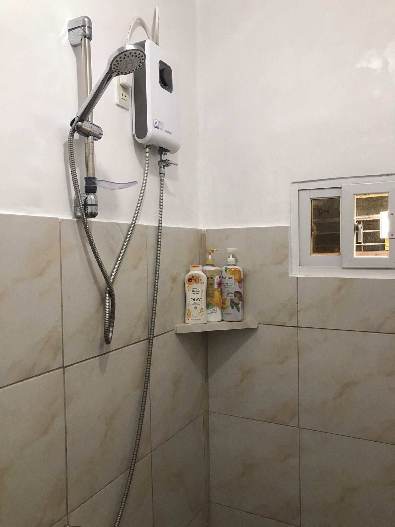 Un espace douche équipé d’un pommeau de douche à main, d’un panneau de commande fixé au mur et d’une étagère pour les articles de toilette.