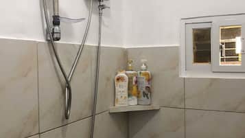 Un espace douche équipé d’un pommeau de douche à main, d’un panneau de commande fixé au mur et d’une étagère pour les articles de toilette.