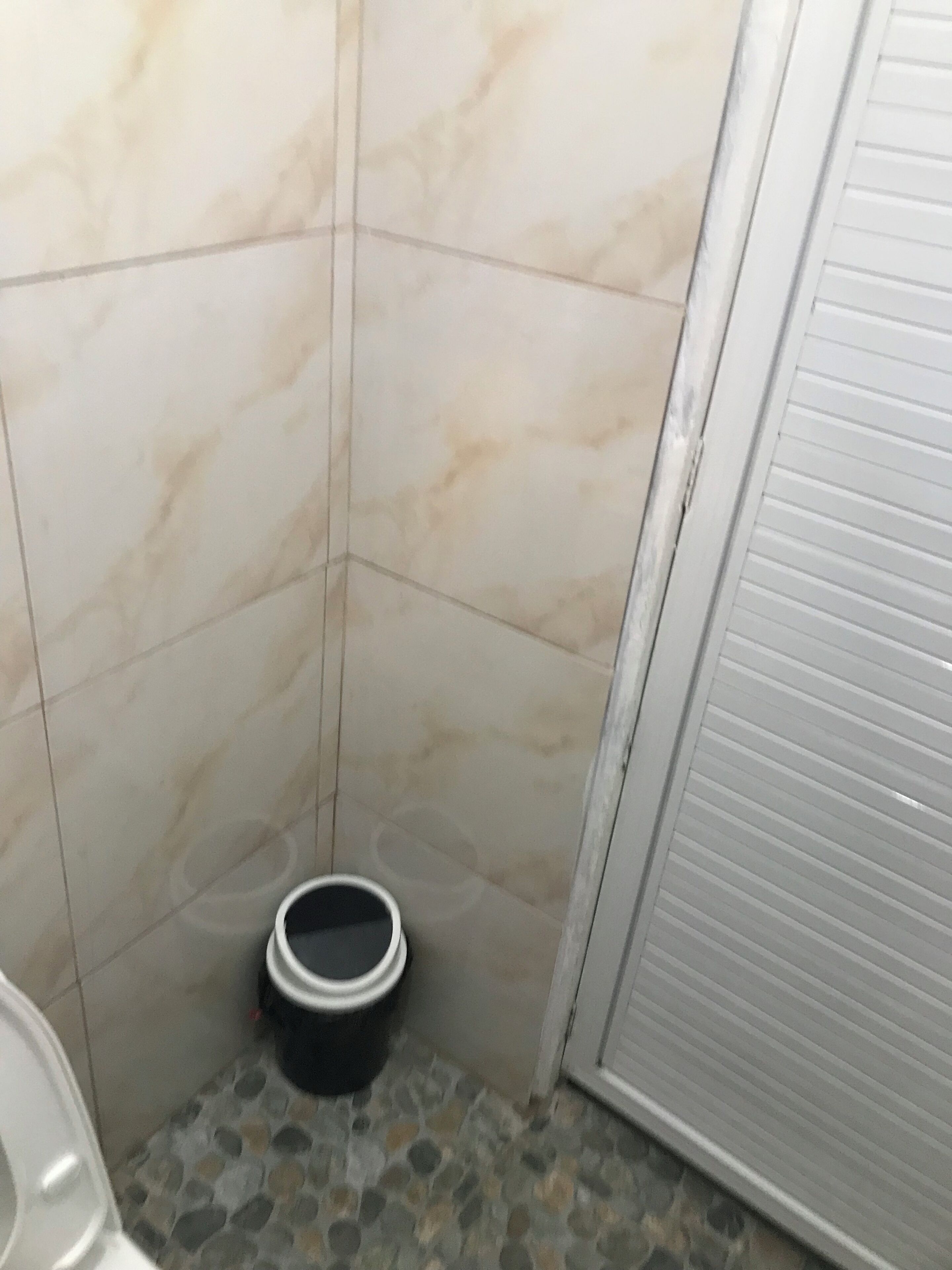 Une salle de bain avec des murs en marbre, un sol en pierre, des toilettes et un seau.