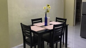 Un comedor con una mesa preparada para cuatro, rodeada de sillas, con dos cuadros en la pared y un florero con flores sobre la mesa.