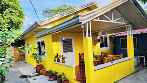 Una casa amarilla con un porche cubierto, plantas en macetas y un pequeño espacio de estar al aire libre.