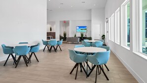 Un hall d’hôtel moderne doté de plusieurs espaces de détente, d’un écran de télévision et de grandes fenêtres.